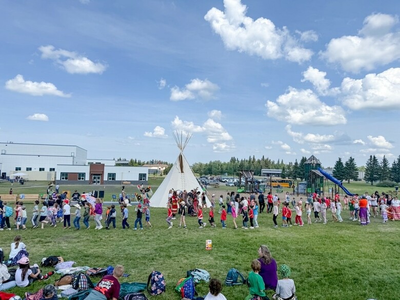 Students participating in a round dance with a tipi