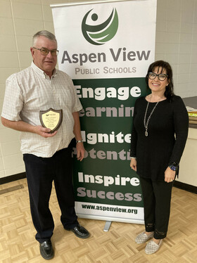 A man receiving an award plaque from a woman, standing in front of a banner