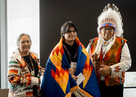 Young man wrapped in Star Blanket with Indigenous Elders